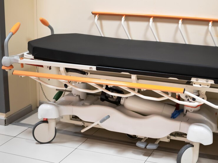 Vista de cerca de una cama o camilla de hospital con el fondo del pasillo