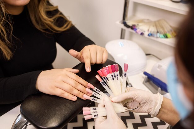 Foto vista de cerca del cliente que elige el color de uñas de la paleta de colores de uñas en el interior del gabinete esteticista