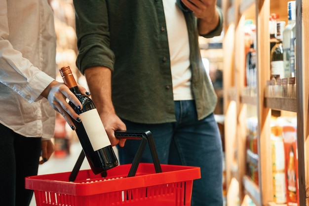 Vista de cerca colocando la botella hecha elección Hombre y mujer están eligiendo vino en la tienda