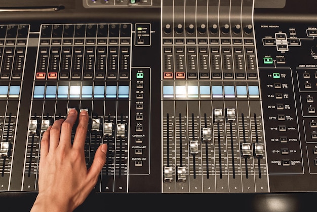 Foto vista de cerca de control de sonido profesional de mano masculina mezclando sonidos en la consola de mezcla de audio digital