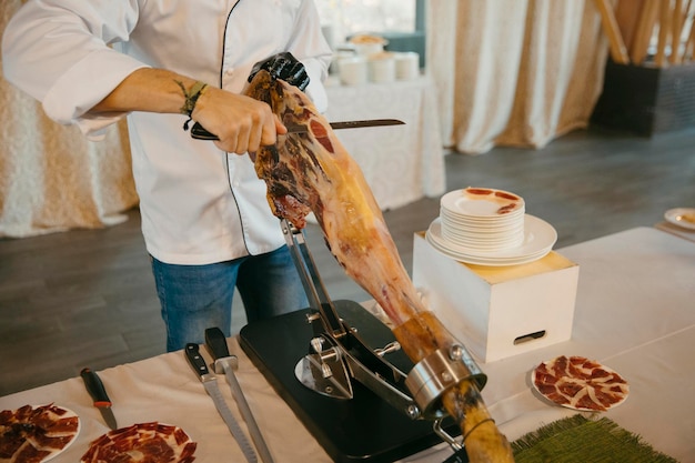 Foto vista de cerca de un cortador de jamón profesional mientras corta el jamón y prepara las porciones.