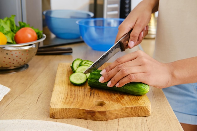 Vista de cerca de cortar pepino para ensalada en tablero de madera