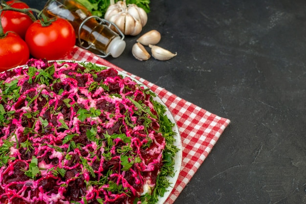 Vista de cerca de una deliciosa ensalada en una toalla despojada de rojo y verduras frescas botella de aceite caído sobre fondo negro