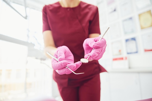 Vista de cerca de una dentista en uniforme que está de pie en la oficina de estomatología con herramientas en las manos