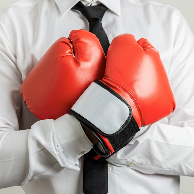 Vista de cerca del empresario con guantes de boxeo rojos con los brazos cruzados sobre el pecho.