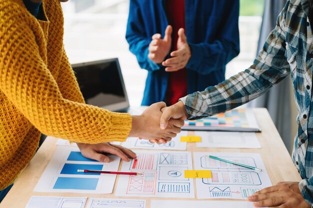 Vista de cerca del equipo de desarrolladores de interfaz de usuario haciendo una lluvia de ideas sobre su proyecto con un teléfono inteligente portátil y una tableta digital Agencia de desarrollo digital creativa en la oficina