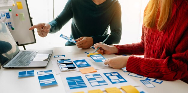 Vista de cerca del equipo de desarrolladores de la interfaz de usuario haciendo una lluvia de ideas sobre su proyecto con un teléfono inteligente portátil y una tableta digital Agencia de desarrollo digital creativa
