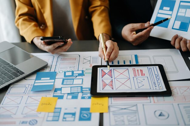 Vista de cerca del equipo de desarrolladores de UI haciendo una lluvia de ideas sobre su proyecto con un teléfono inteligente portátil y una tableta digital Agencia de desarrollo digital creativa con íconos virtuales