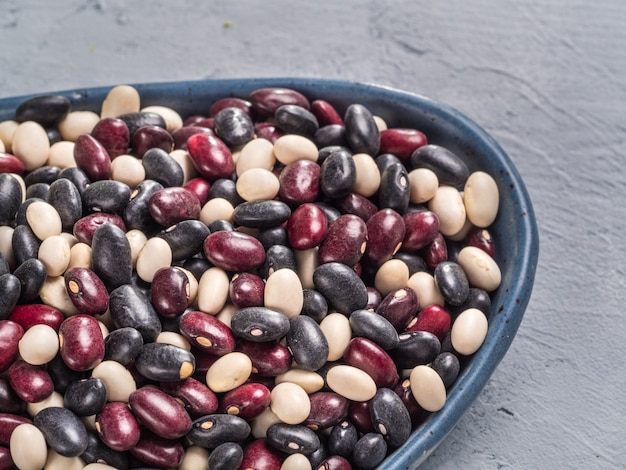 Vista de cerca de frijoles crudos mezclados en placa azul sobre fondo de hormigón gris mezclado de frijoles rojos y blancos negros con espacio de copia