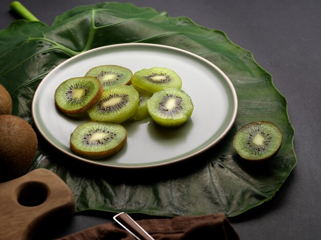 Vista de cerca de la fruta de kiwi fresca en rodajas en un plato decorado con hojas verdes en la mesa de la cocina