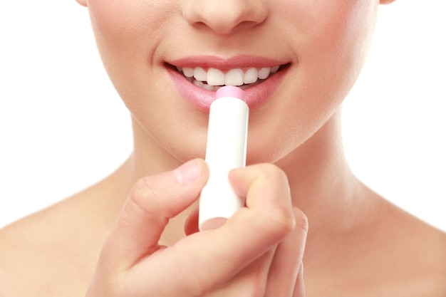 Vista de cerca de la hermosa joven aplicando lápiz labial, fondo blanco.
