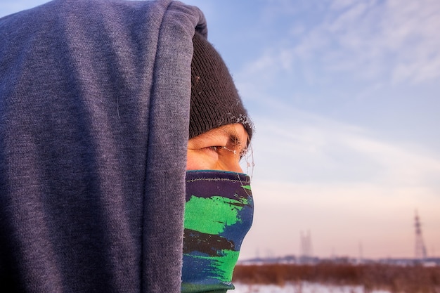 Vista de cerca de un hombre caucásico facewith bufanda como máscara y chaqueta de invierno con capucha.