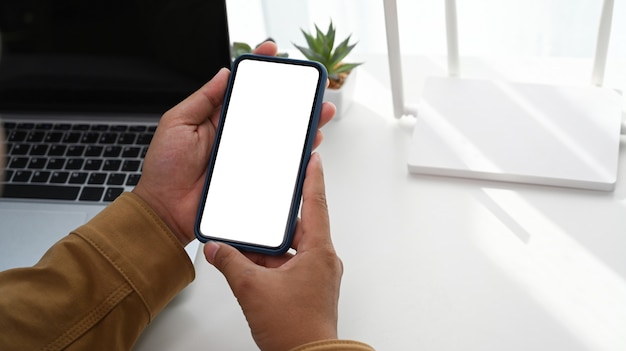 Vista de cerca del hombre usando un teléfono inteligente y sentado frente al enrutador inalámbrico en la oficina en casa.