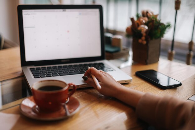 Vista de cerca de irreconocible está trabajando en una computadora portátil moderna que mira en la pantalla del monitor en un café acogedor Taza de café en la mesa