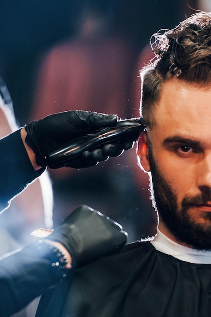 Foto vista de cerca del joven barbudo que se sienta y se corta el pelo en la peluquería