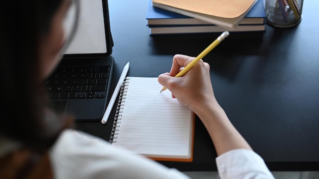 Vista de cerca de la joven empresaria con tableta de computadora y escribiendo en el cuaderno vacío.