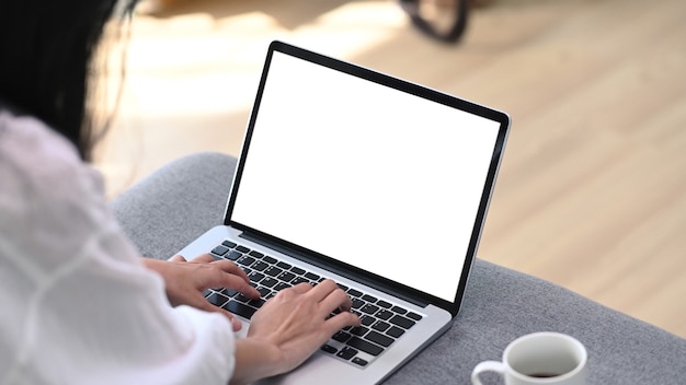 Vista de cerca de la joven freelance trabajando con computadora portátil mientras está sentado en el sofá en la sala de estar