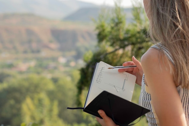 Vista de cerca de una joven irreconocible dibujando en su cuaderno y un entorno natural