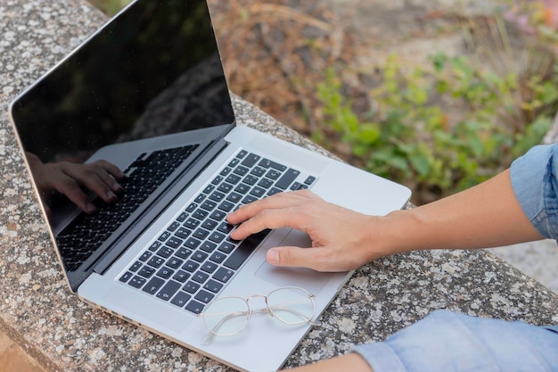 Vista de cerca de un joven irreconocible que trabaja en su computadora portátil con la mano y anteojos encima