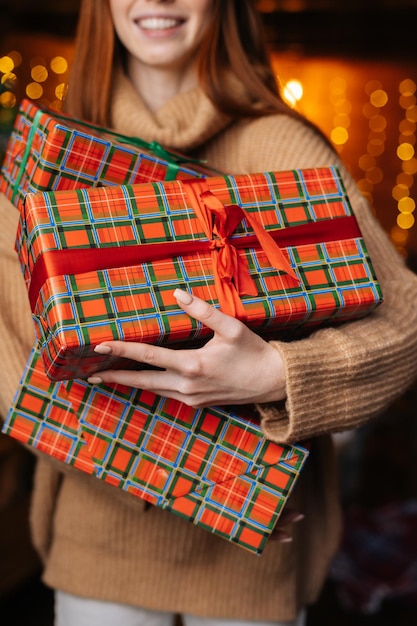 Vista de cerca de una joven pelirroja sonriente sosteniendo muchas hermosas cajas de regalo de Navidad