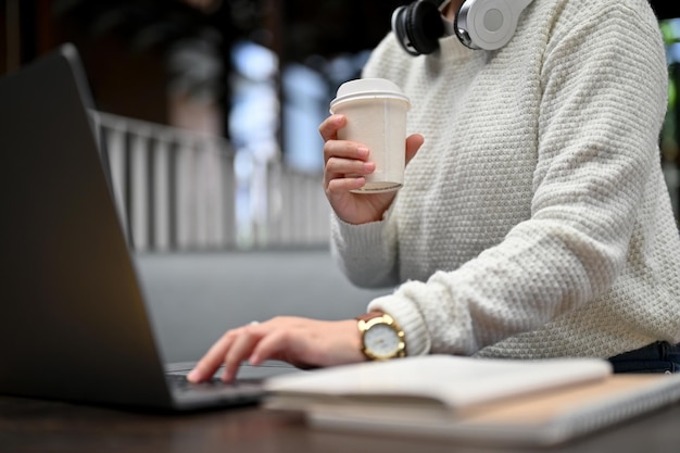 Vista de cerca de una joven que trabaja en un café escribiendo una laptop y bebiendo café