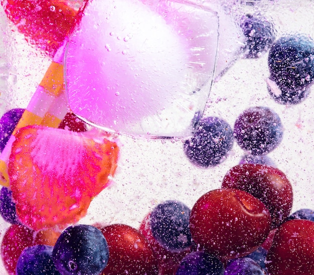 Foto vista de cerca de la limonada fría y fresca con bayas brillantes y cubitos de hielo en luz de neón. textura de refrescante bebida de verano con macro burbujas en vidrio. efervescente o flotando hasta la parte superior de la superficie.