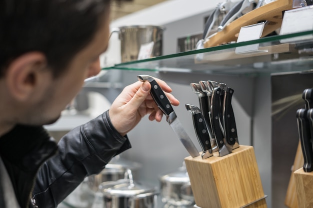 Vista de cerca de la mano del cliente eligiendo juego de cuchillos para cocina. El esta guardando un cuchillo