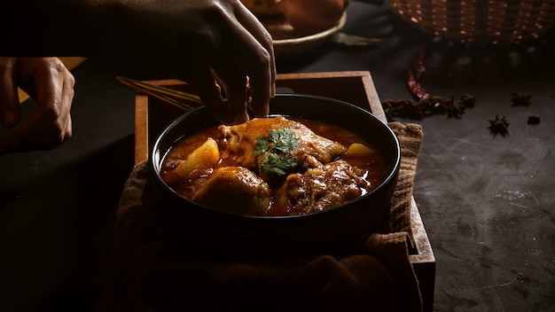 Vista de cerca de la mano femenina cocinar pollo al curry Massaman para servir en el restaurante tailandés