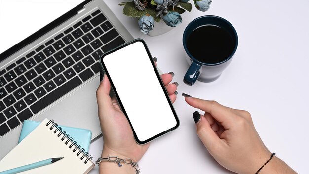 Vista de cerca de la mano de la mujer usando un teléfono inteligente en el escritorio de la oficina blanca