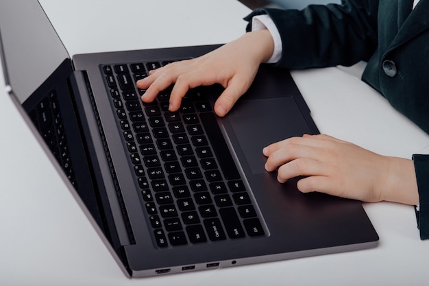 Vista de cerca de la mano del niño escribiendo en la computadora portátil en la vista superior de la mesa