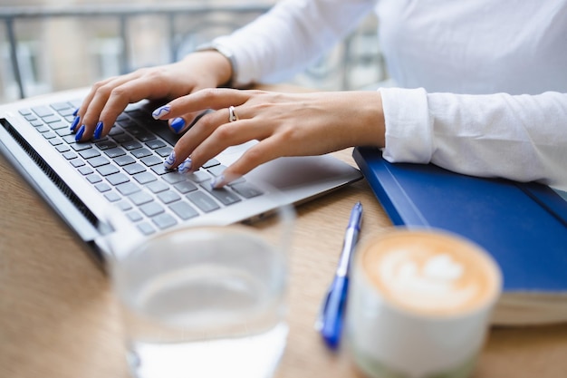 Vista de cerca de las manos de una chica escribiendo en un teclado portátil en la mesa de un café