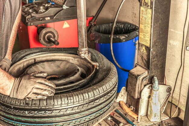 Vista de cerca de las manos con guantes de un mecánico reparando un neumático en un garaje sucio