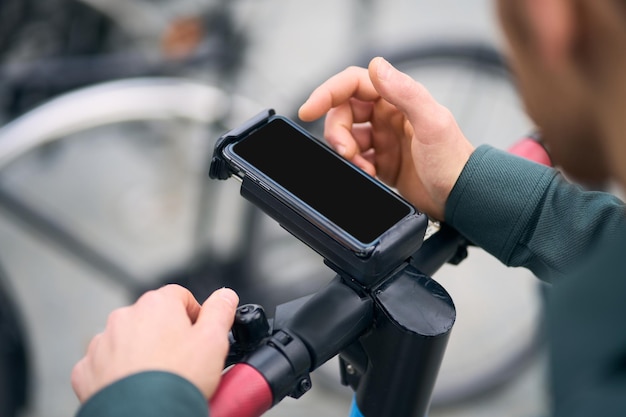 Vista de cerca de las manos del hombre desconocido usando el teléfono móvil mientras se desbloquea el scooter