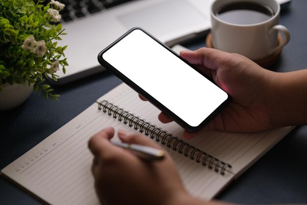 Vista de cerca de las manos del joven usando un teléfono inteligente mientras está sentado en la oficina en casa