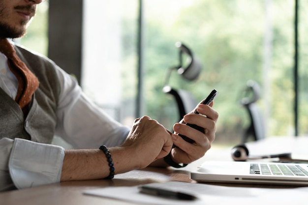 Foto vista de cerca de las manos masculinas tocando el teléfono móvil hombre de mediana edad usando un teléfono inteligente mientras está sentado en su escritorio en la oficina