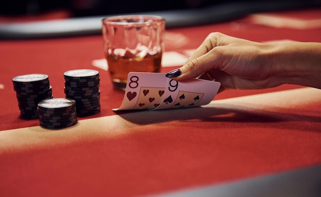 Vista de cerca de las manos de la mujer. Niña juega al juego de póquer por mesa en el casino y chequea las cartas