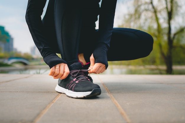 Foto vista de cerca de las manos de la mujer en traje deportivo atarse los cordones de sus zapatillas deportivas mientras se ejecuta en el parque