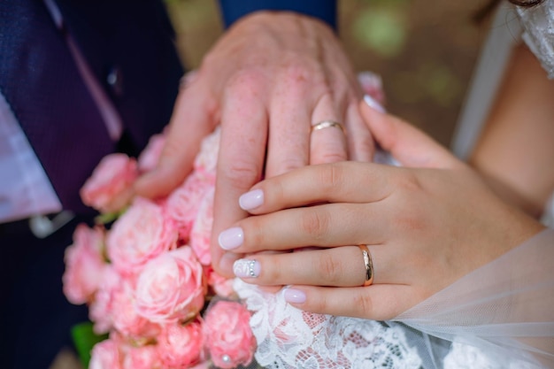 Vista de cerca de las manos de los recién casados sosteniendo un colorido ramo de novia para el novio y la novia con rin de boda