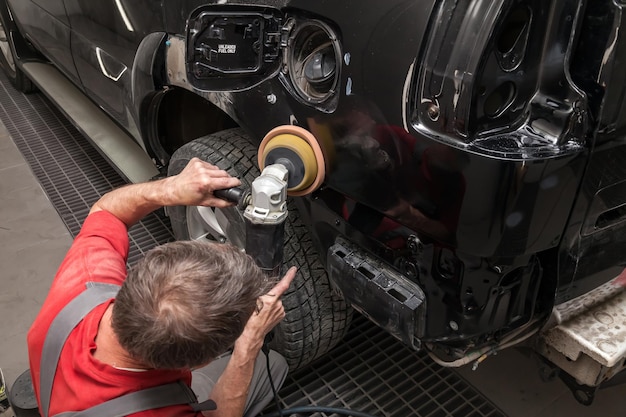 Vista de cerca de las manos de un trabajador masculino que sostiene una herramienta para pulir el guardabarros de un automóvil mientras trabaja en un taller de detalles de vehículos Industria de servicios automotrices