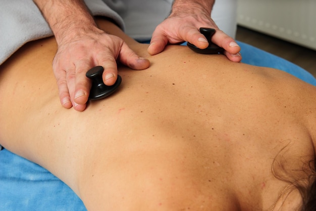 Vista de cerca del masajista masculino masajeando la espalda y los omóplatos de la mujer acostada en la mesa de masaje en el salón de spa Hermosa mujer joven con una piel perfecta recibiendo un masaje relajante