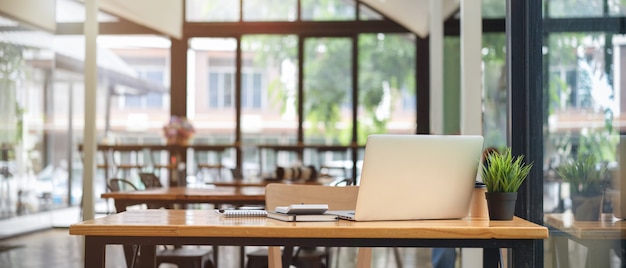 Vista de cerca de la mesa de espacio de coworking en el café con un portátil y un interior borroso en el fondo