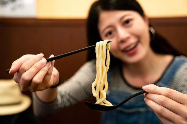 la vista de cerca de una mujer joven comiendo con palillos y cuchara en un restaurante japonés en osaka.