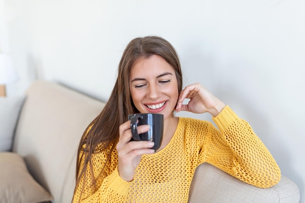 Vista de cerca de una mujer joven con una taza de bebida caliente en el espacio en blanco en casa Personas bebidas y concepto de ocio mujer joven feliz con una taza de té o café en casa