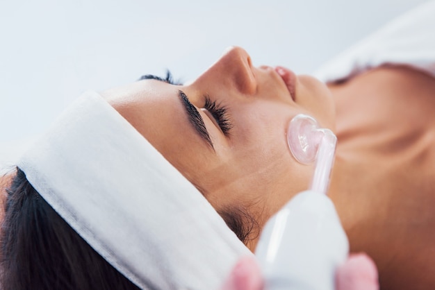 Vista de cerca de la mujer que está acostada en el salón de spa y tiene un procedimiento de limpieza facial mediante el uso de un dispositivo moderno.