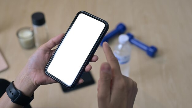 Vista de cerca de una mujer sentada en una alfombra y usando un teléfono inteligente descansando de los ejercicios en casa