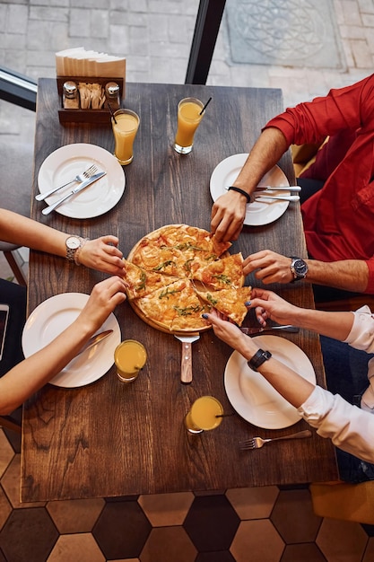 Vista de cerca de las personas que toman y comen pizza juntos en el interior.