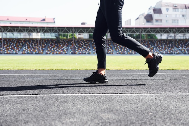 Vista de cerca de las piernas del corredor con pantalones negros y zapatos que están al aire libre en la pista