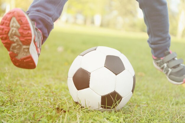 Foto vista de cerca de las piernas del niño y la pelota sobre la hierba verde