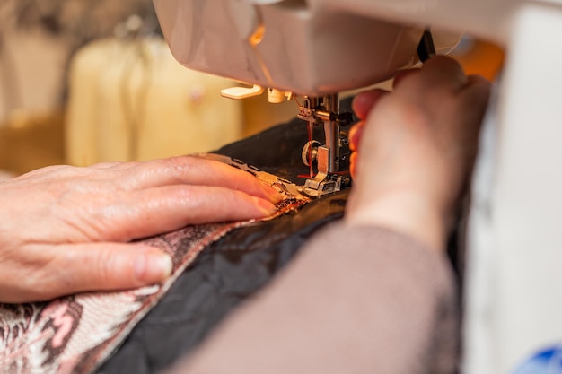 Una vista de cerca del proceso de costura de la mano de una anciana usando la técnica de enfoque selectivo de la máquina de coser