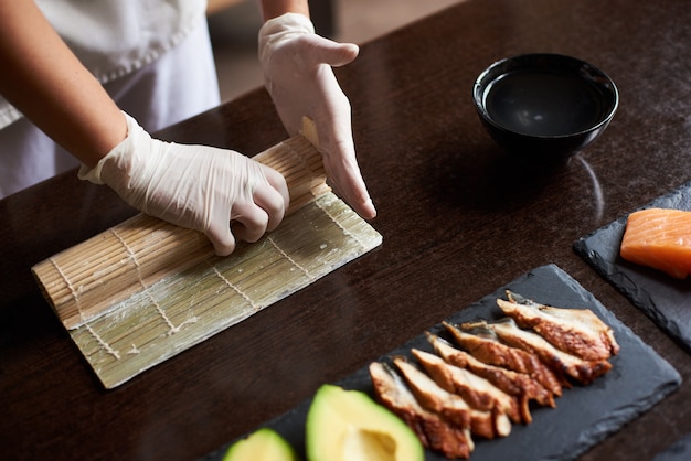 Vista de cerca del proceso de preparación de sushi de laminación. Manos del maestro haciendo un rollo de sushi con estera de bambú.